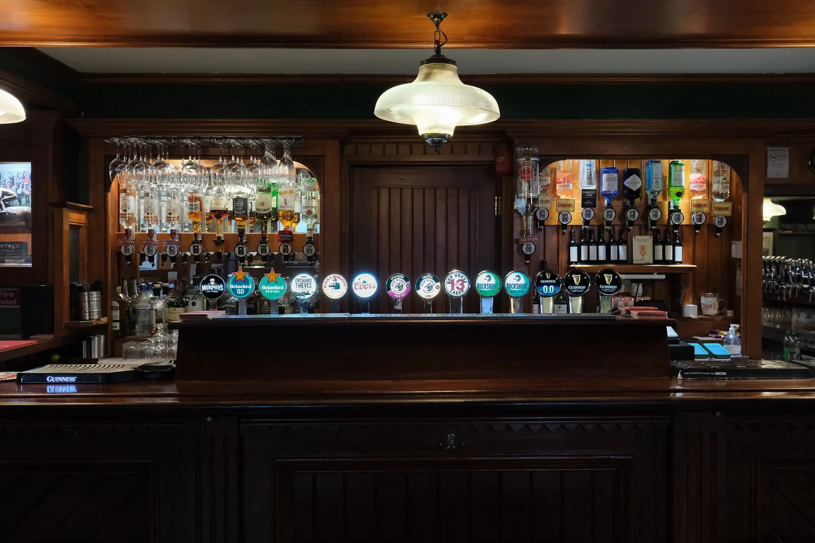 The back bar: a row of lit beer taps beneath a glass pendant lamp, with wooden shelves of spirits on either side