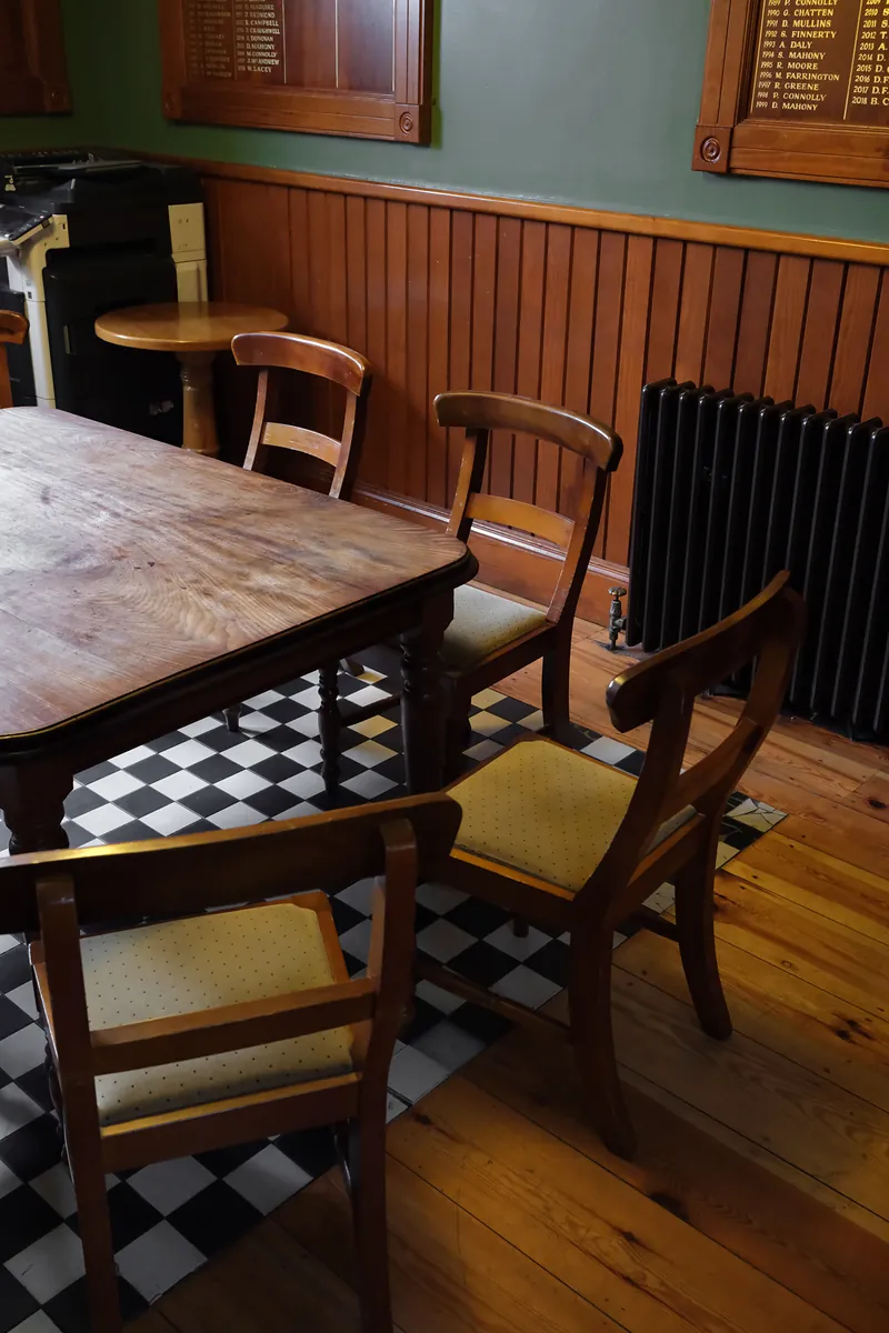 A wooden table and chairs on a black and white checkerboard floor, with gilded honours boards on a green wall