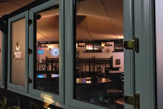 The beer garden after dark, seen through its windows, warmly lit with neon signs on the wall