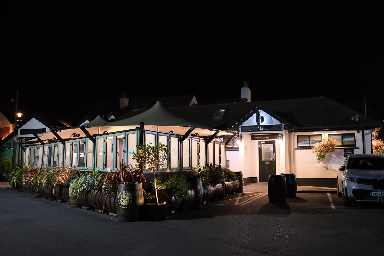 Jas. Manzor. at night: the lamplit Lounge entrance and covered beer garden under a black sky