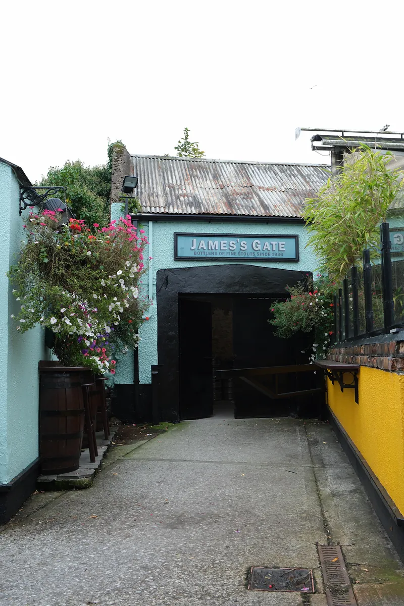 A flower-lined lane leading to a doorway under a sign reading James’s Gate, Bottlers of Fine Stouts since 1936