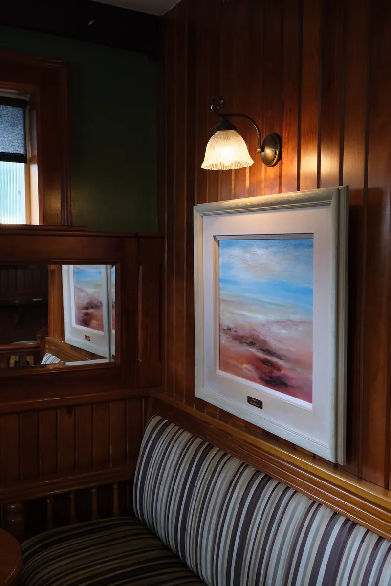 A striped banquette beneath a framed painting and a glass wall lamp, set in wood panelling