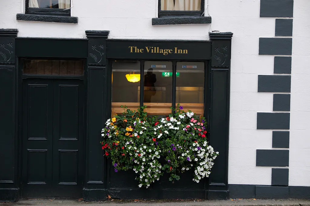The dark-painted Village Inn shopfront on Main Street, gold lettering above a window box overflowing with flowers
