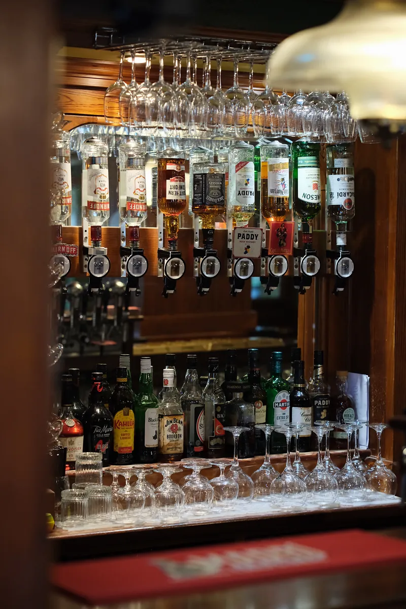 Rows of spirit bottles on optics and hanging wine glasses, lit warmly behind the bar